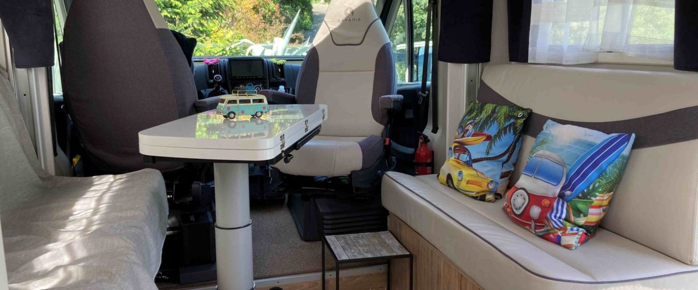 Intérieur d'un van aménagé avec des coussins colorés, table et sièges confortables.