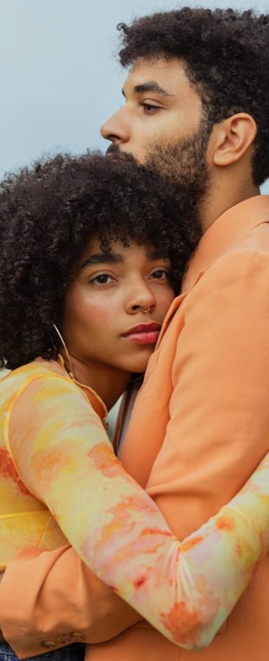 Un couple se serre dans les bras, avec des vêtements aux teintes douces.